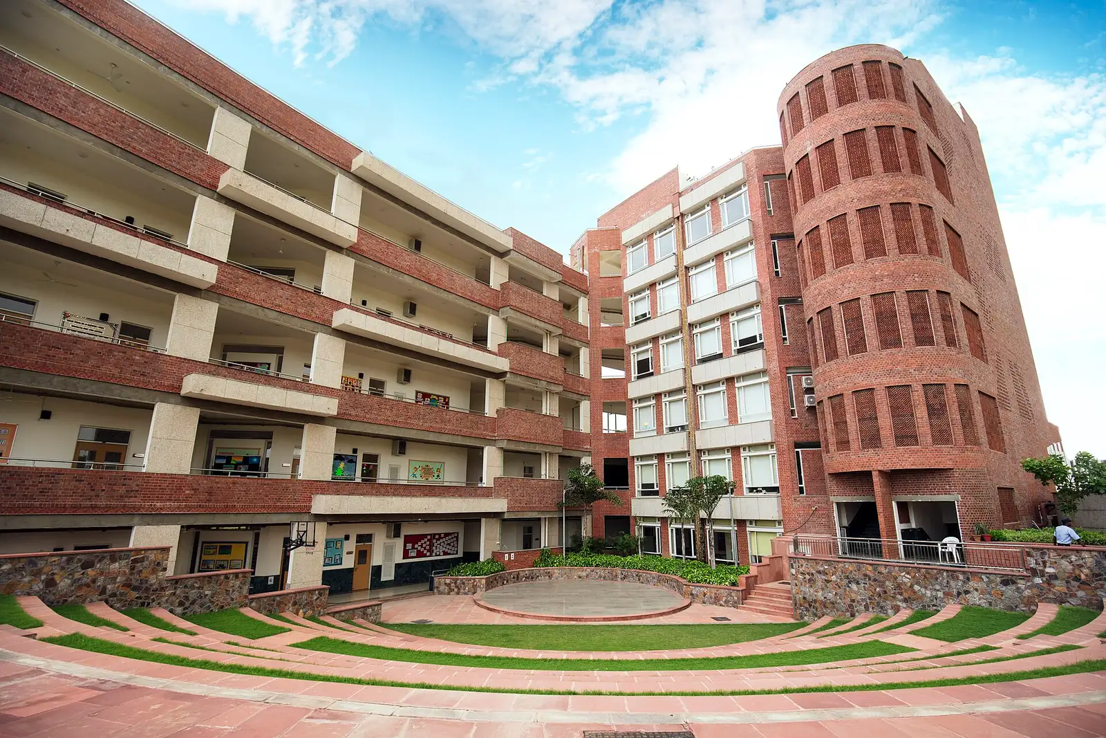 A red brick school building around a stepped lawn courtyard, under a blue sky
